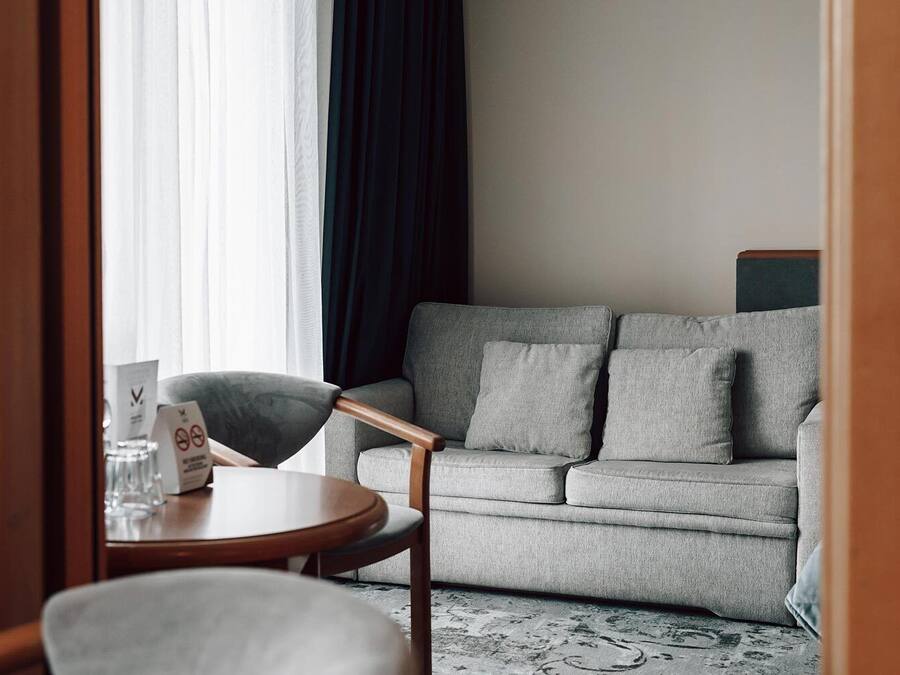 Una habitación de hotel moderna con un sofá gris, una silla de madera y una pequeña mesa redonda.