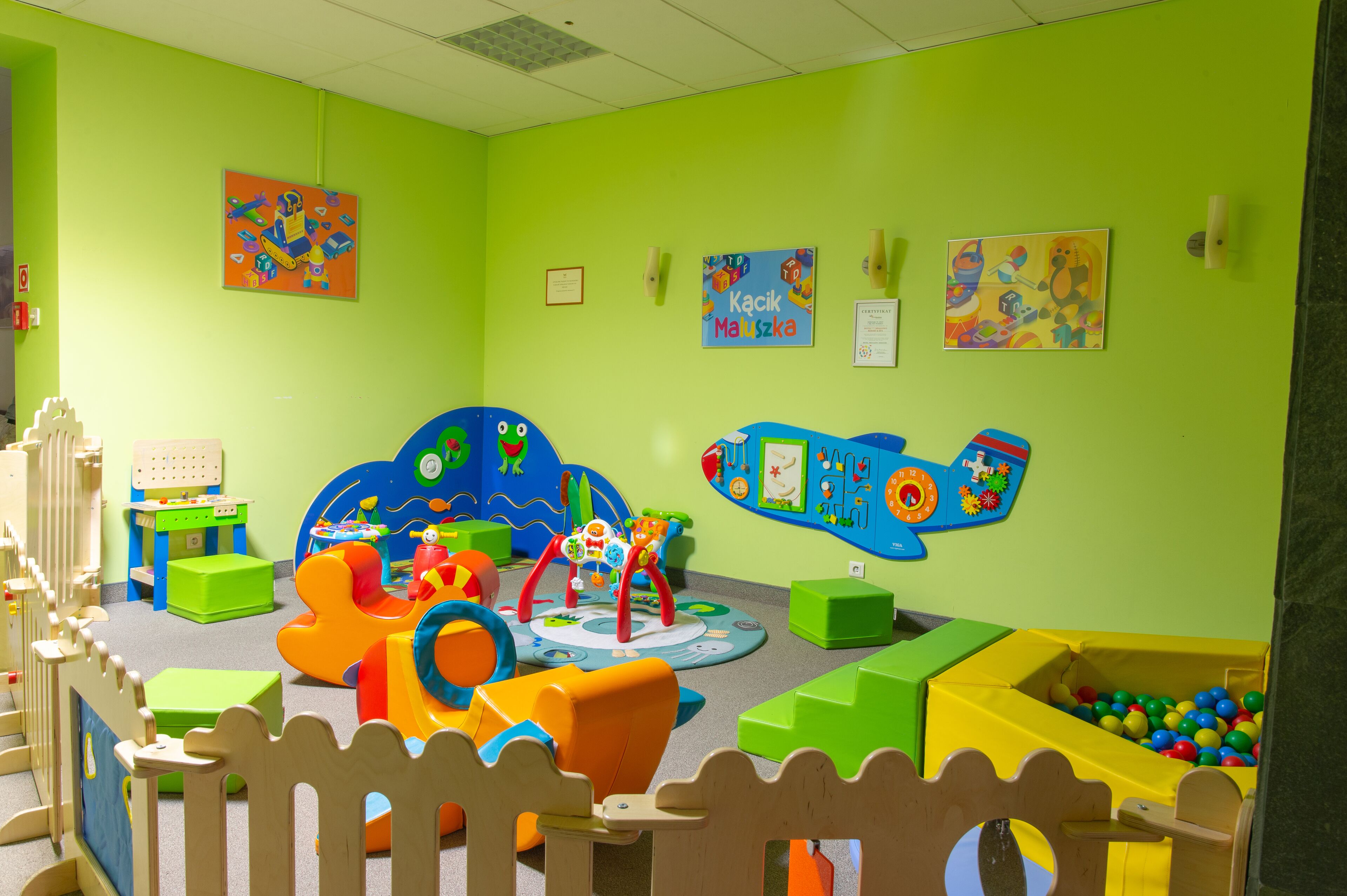 Un salón de juegos lleno de color, con una zona de juegos suave, una estructura de juego grande en azul y un pozo de pelotas.