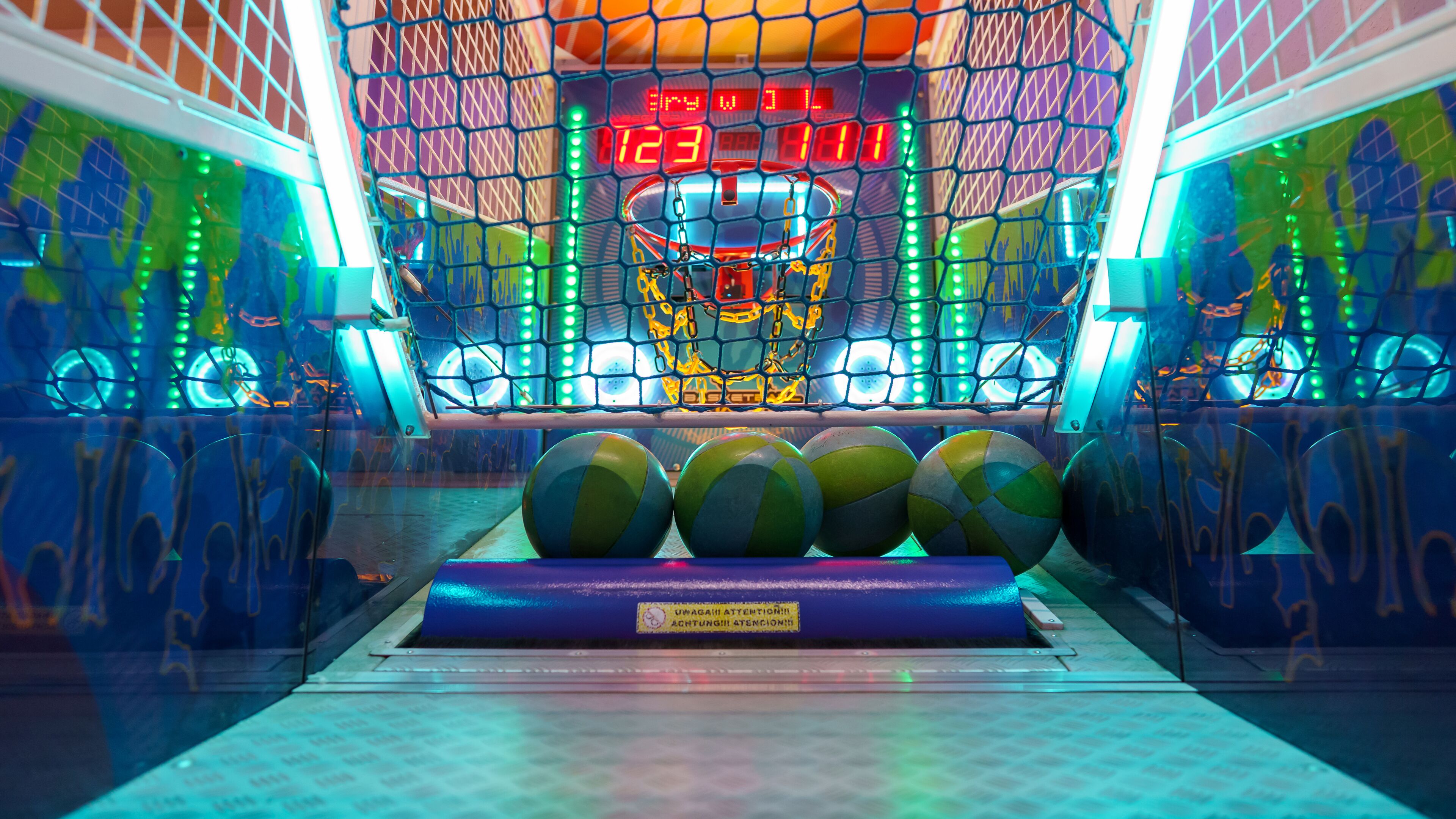 Una cancha de baloncesto con un marcador digital, varias pelotas de baloncesto y un letrero de advertencia de seguridad.