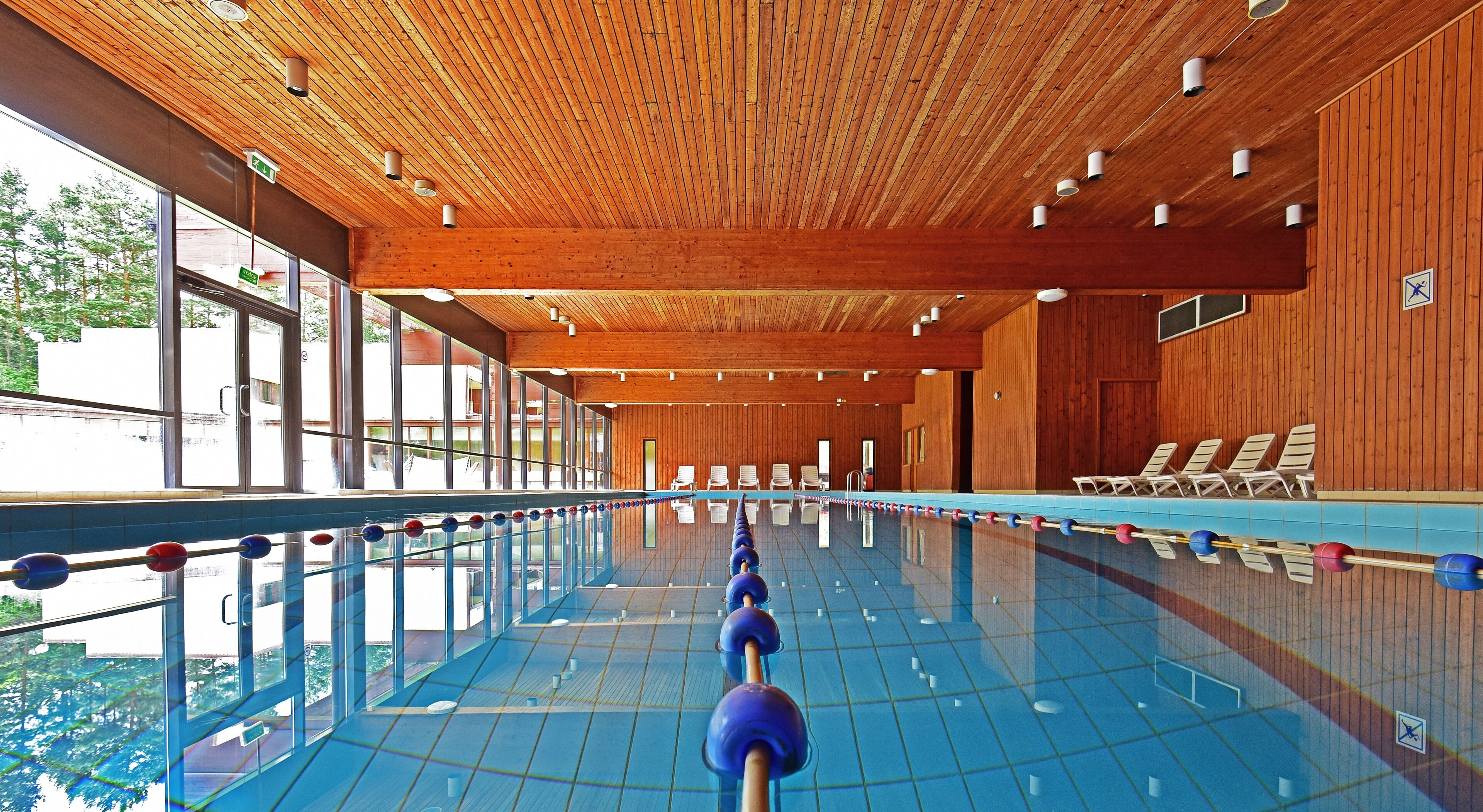 An indoor swimming pool with wooden paneling, clear glass windows, and lounge chairs along the side.