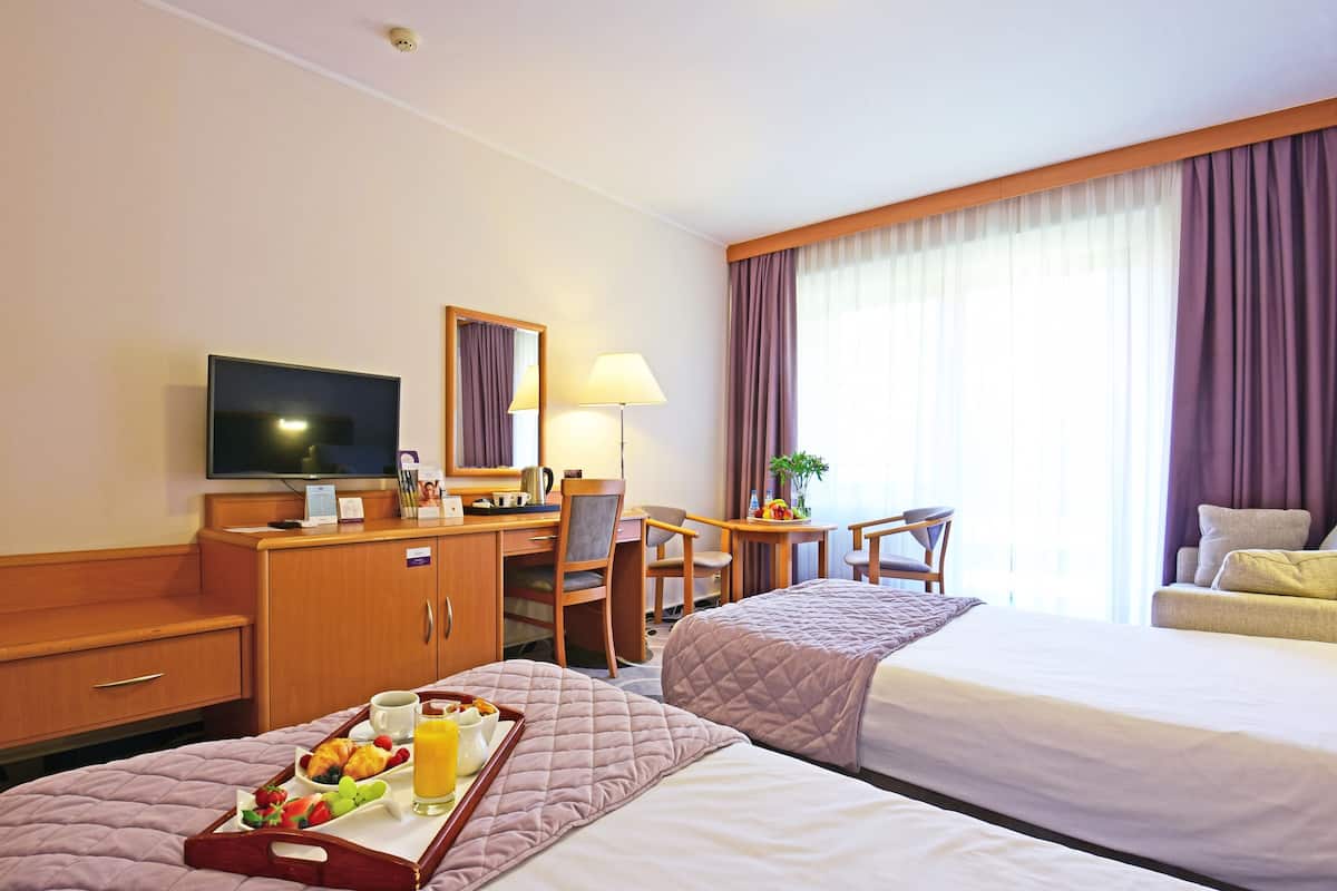 A hotel room with two beds, a desk, a TV, and a breakfast tray on the bed.