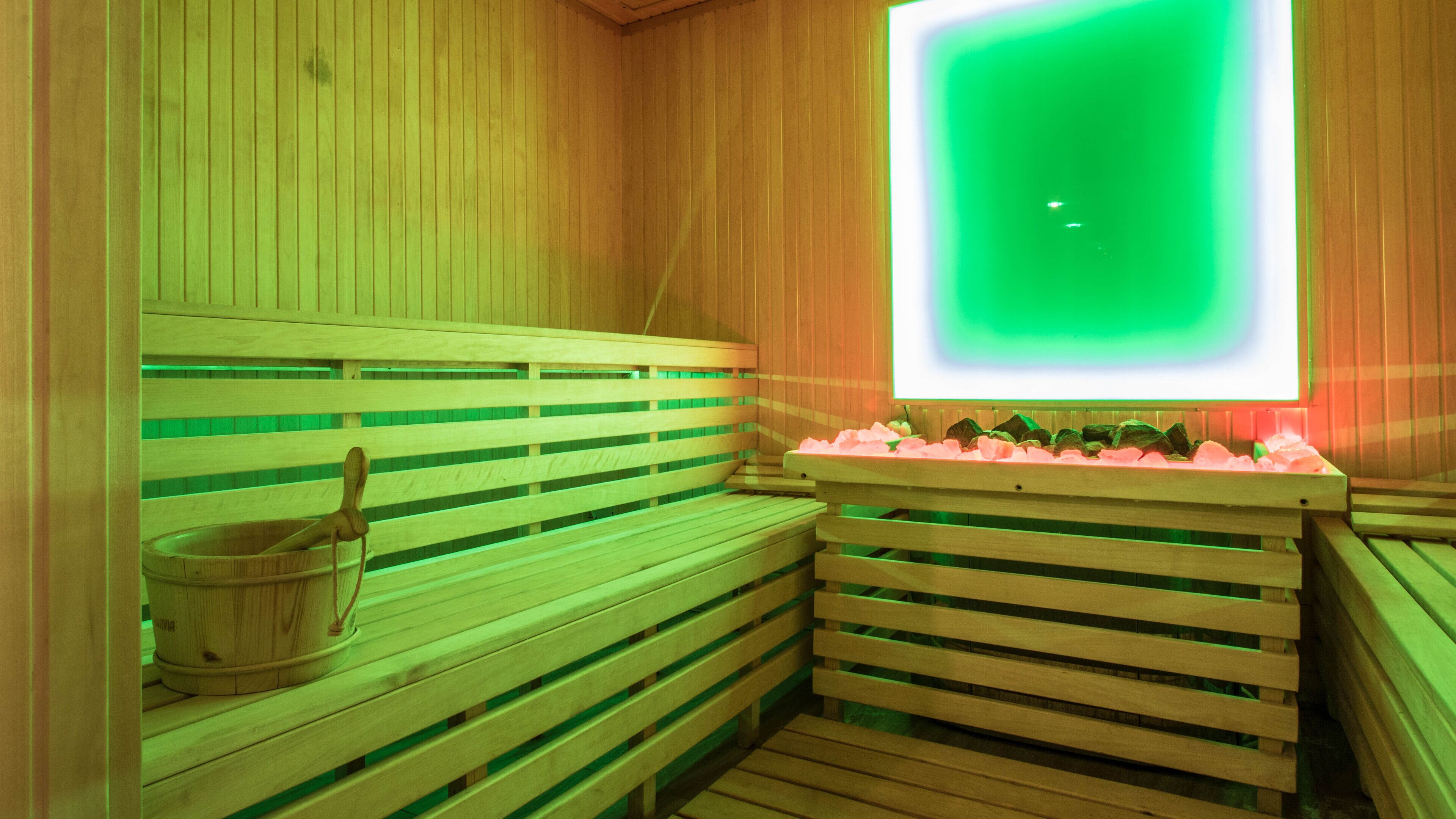 A sauna with wooden benches and a large green-lit wall.