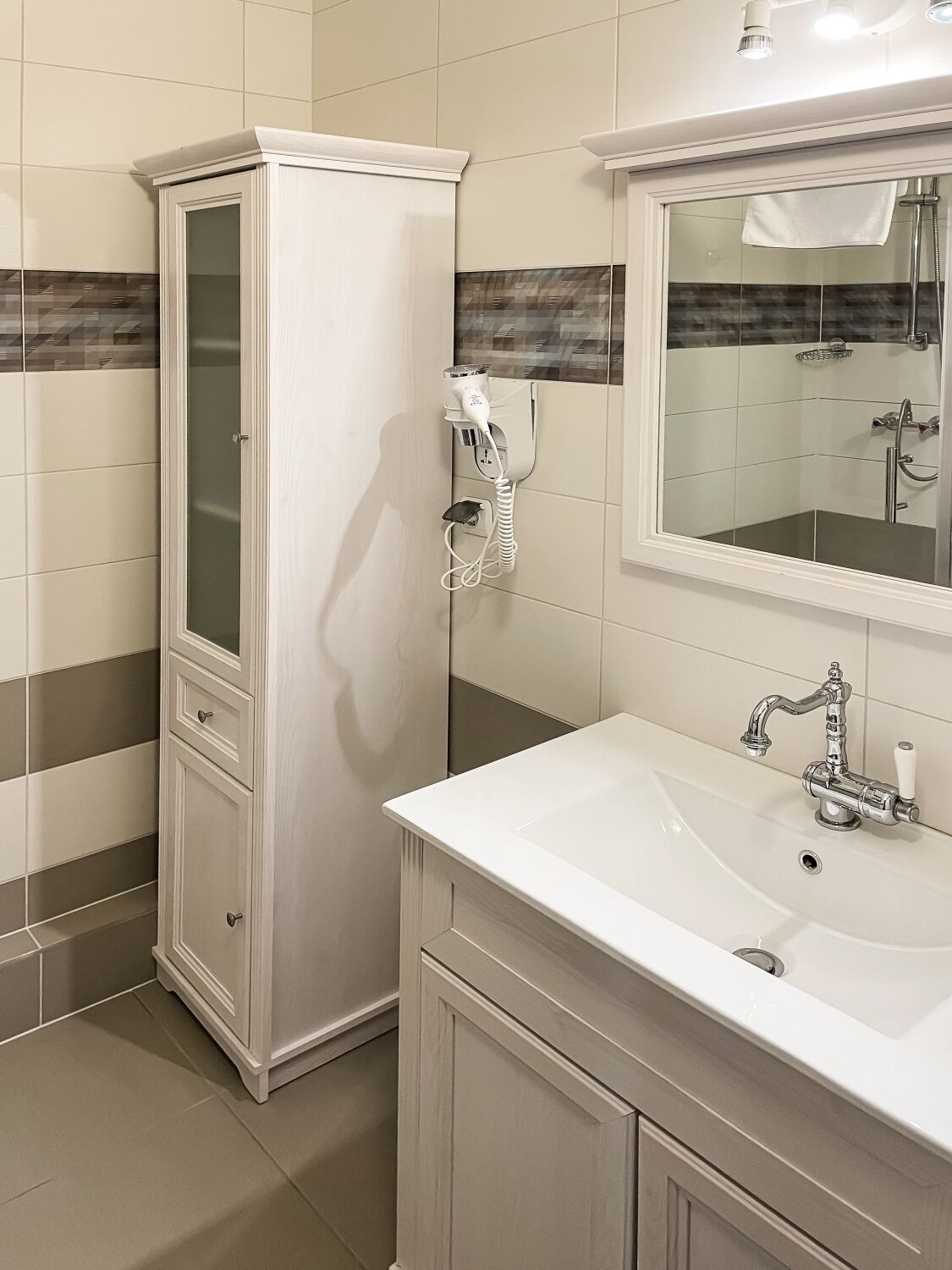 A bathroom with a white cabinet, a sink with a mirror above it, and a shower area.