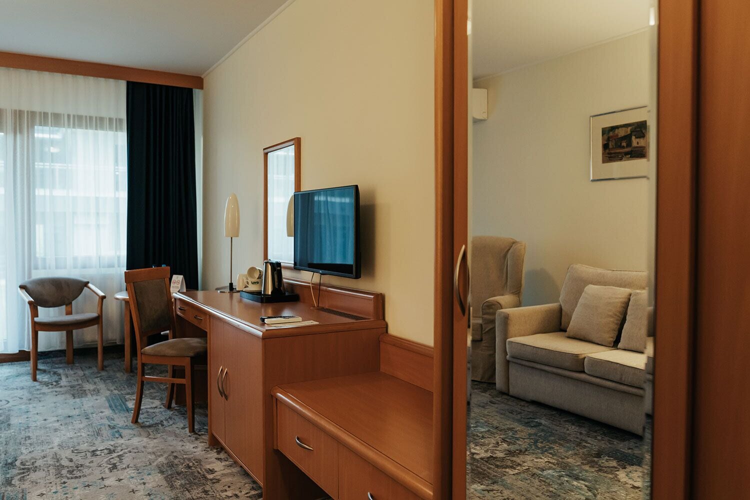 Habitación de hotel con escritorio de madera, televisión, sofá y ventana con cortinas.
