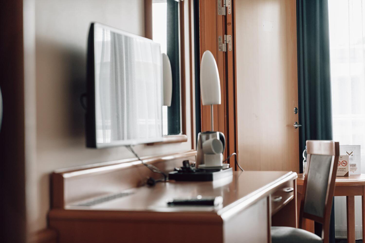 Een hotelkamer met een houten bureau, een flatscreen televisie aan de muur, een lamp en een stoel.