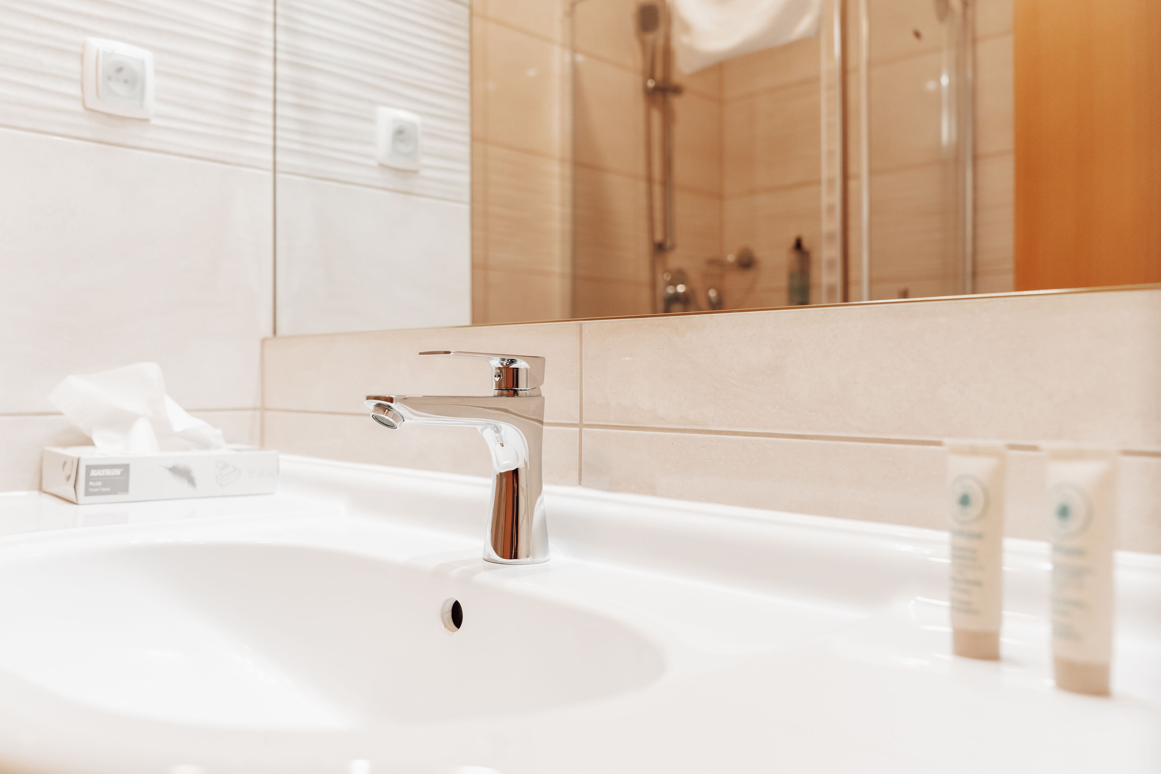 A bathroom with a white sink, chrome faucet, and a mirror reflecting a shower area.