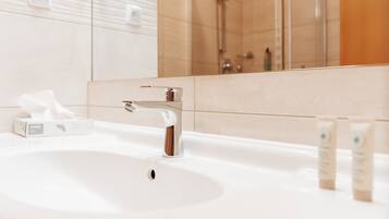 A bathroom with a white sink, chrome faucet, and a mirror reflecting a shower area.