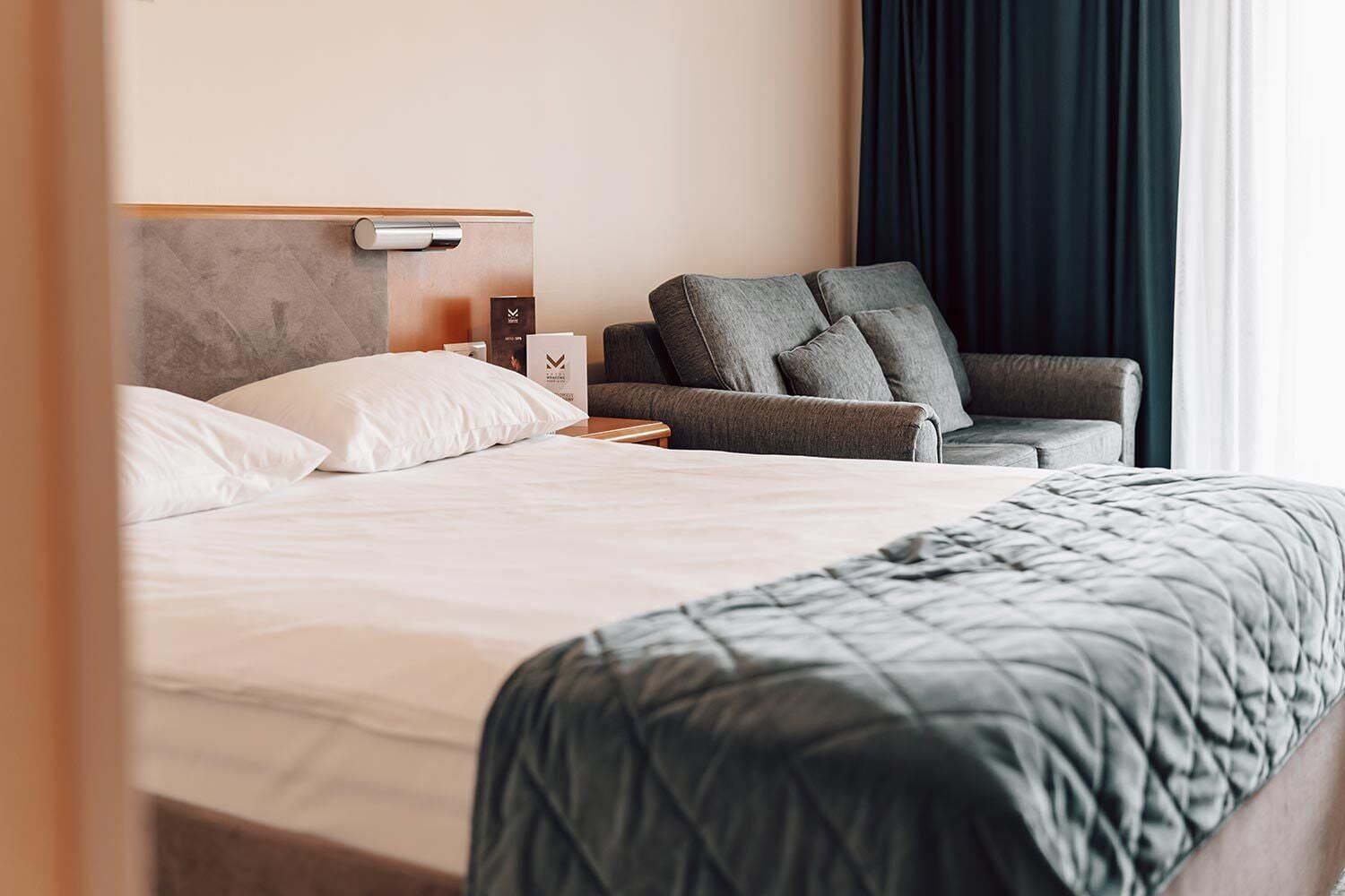 Hotellihuone, jossa on sänky, sohva, yöpöytä ja ikkuna, jossa on verhot.