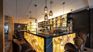 Zona de bar con mostrador de mármol, varias lámparas colgantes y una variedad de botellas y vasos en estantes.