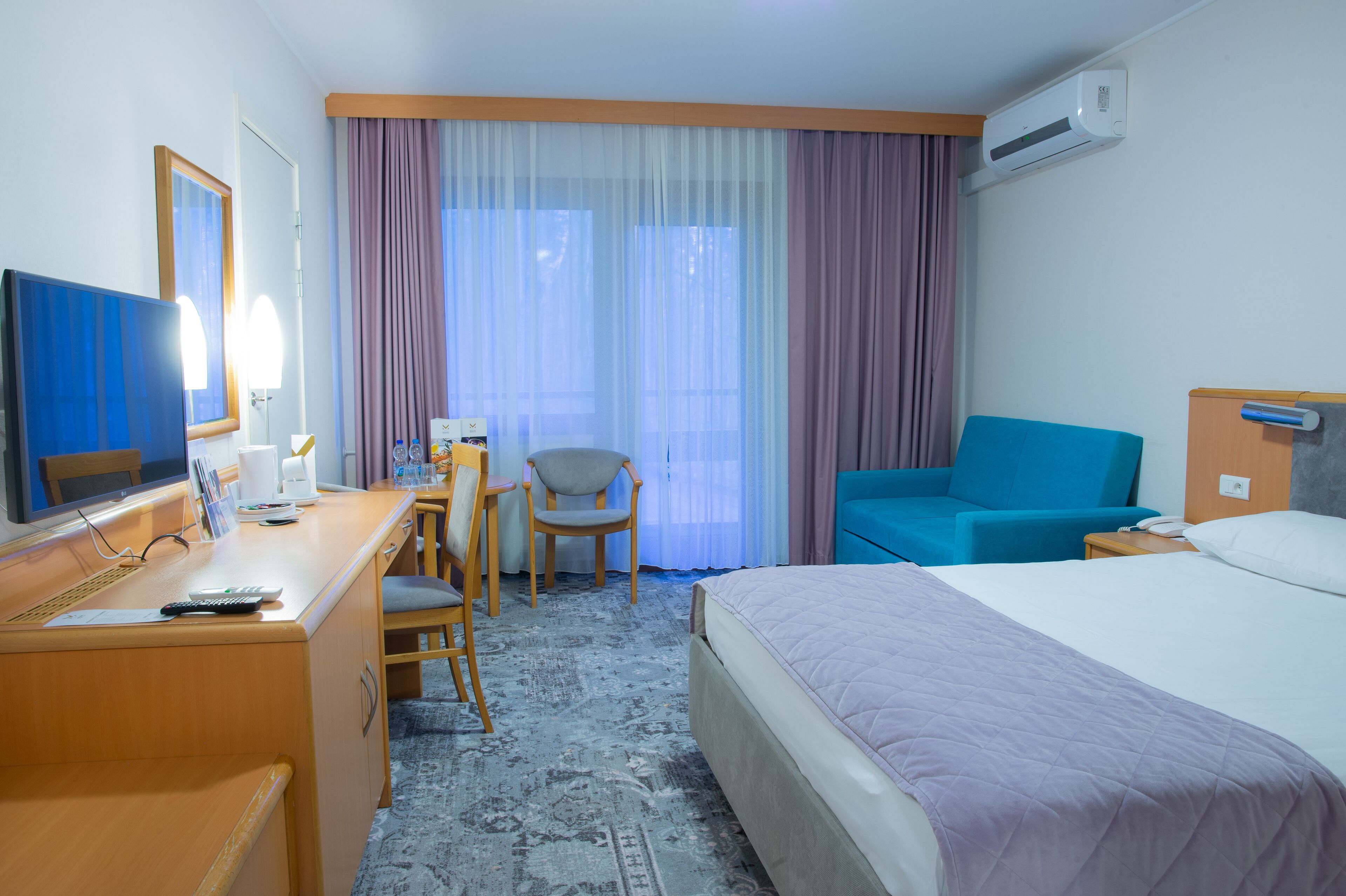 Una habitación de hotel con una cama, un escritorio con una computadora, una silla y un sofá.