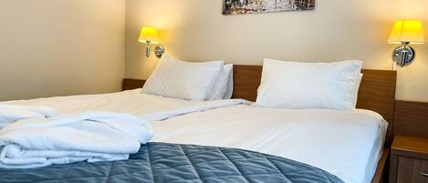 A neatly made bed with a blue quilt, white pillows, and a white blanket folded at the foot. There are two wall-mounted lamps on either side of the bed.