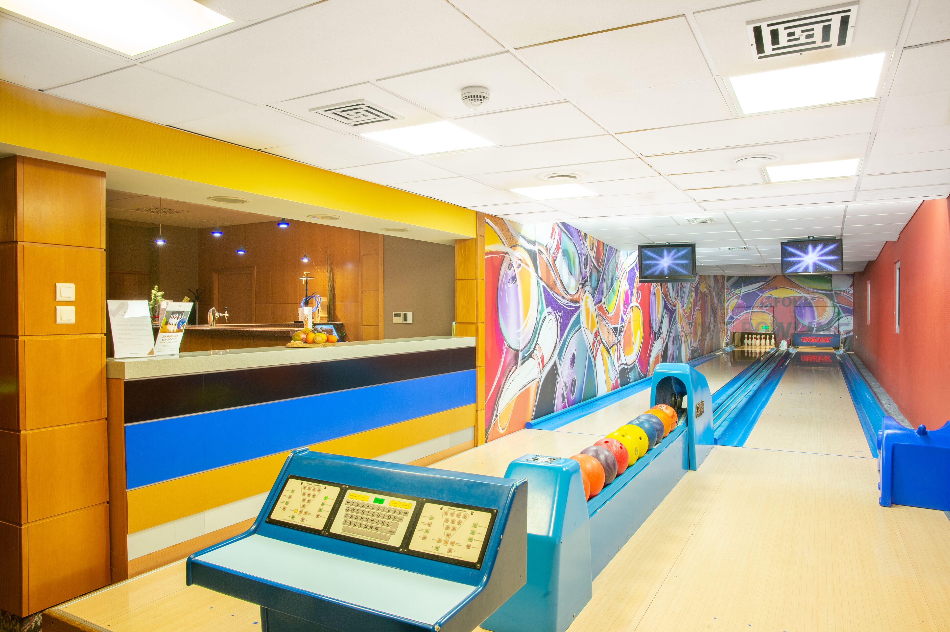 A bowling alley with a reception desk, colorful murals, and a bowling lane.