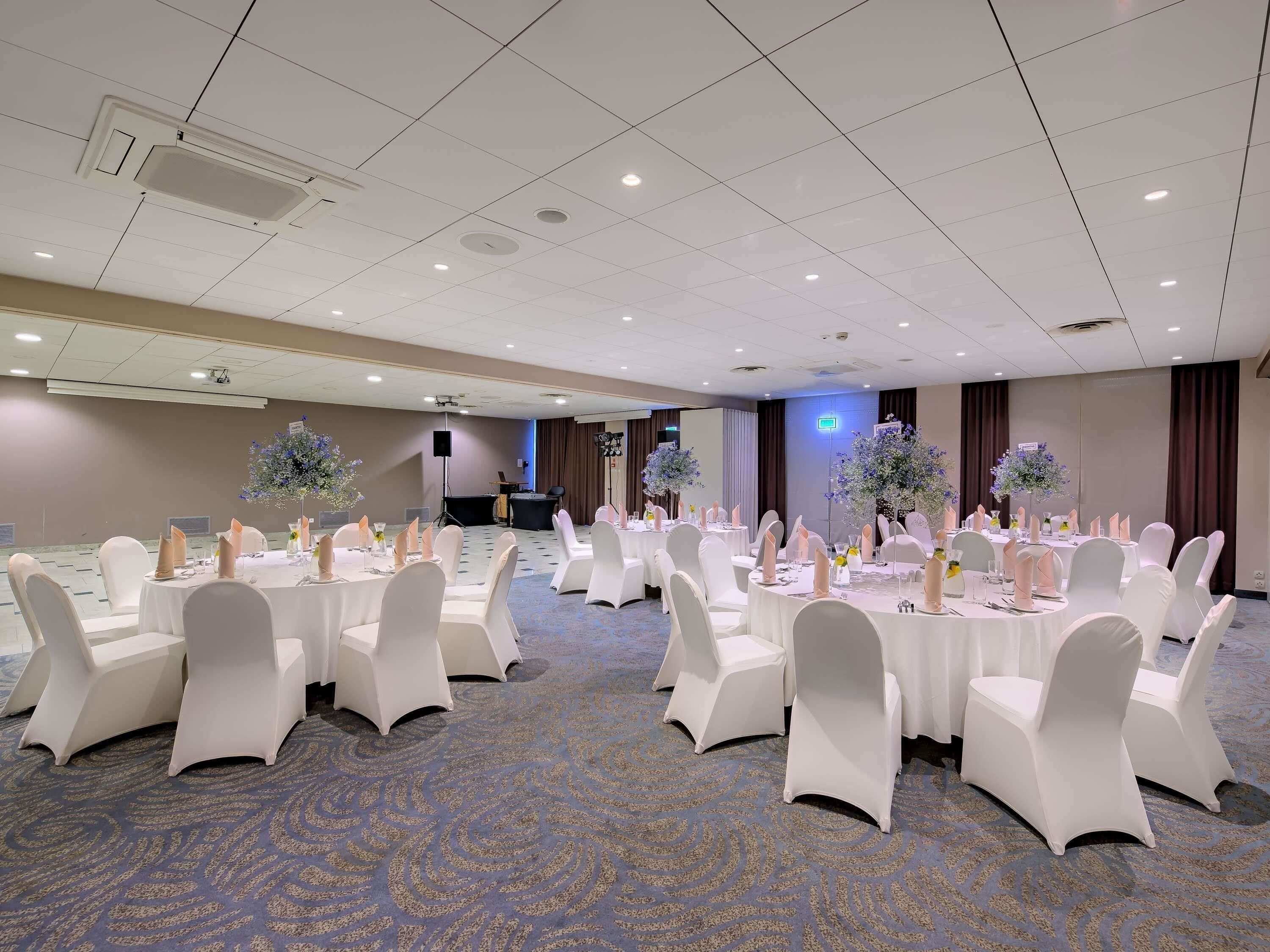 A conference room with round tables, white chairs, and floral centerpieces.
