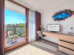 Ett hotellrum med en balkong, ett skrivbord, en stol, en tv och en tavla.
