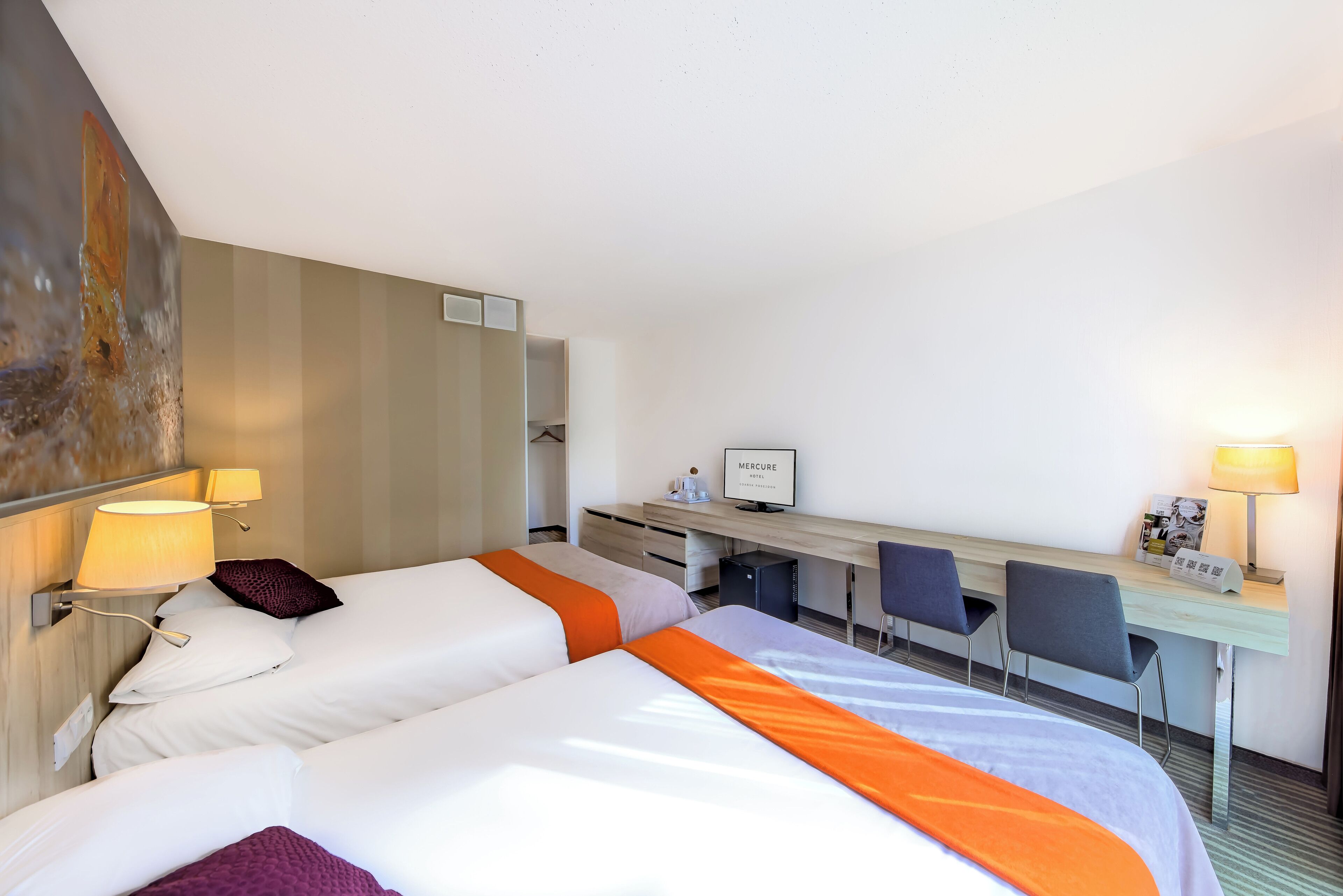 A hotel room with two beds, a desk, chairs, and a computer.