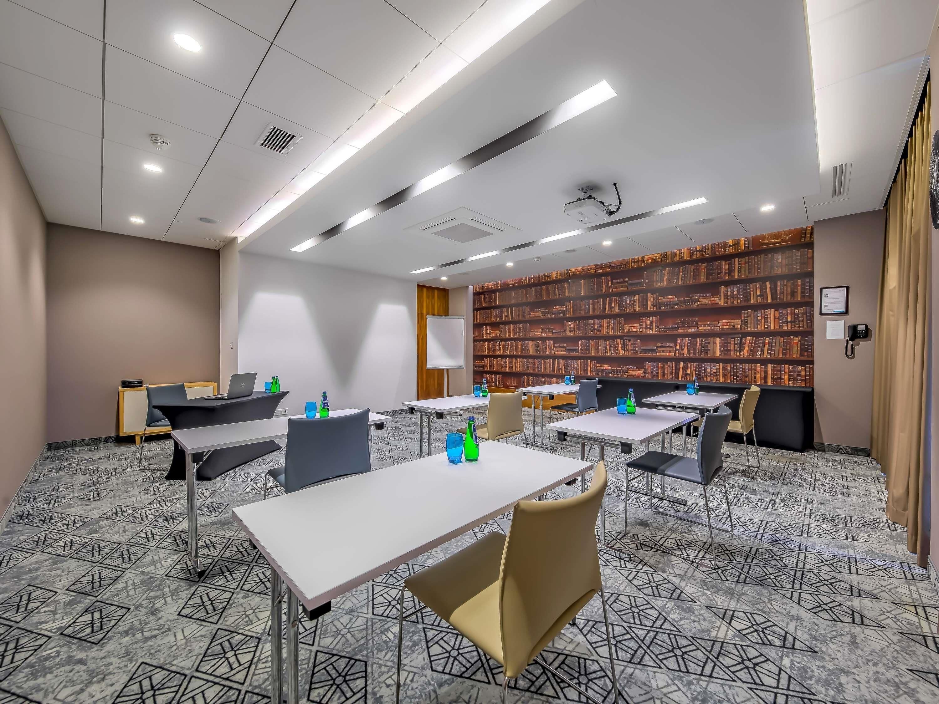 A conference room with tables, chairs, a whiteboard, and a bookshelf.