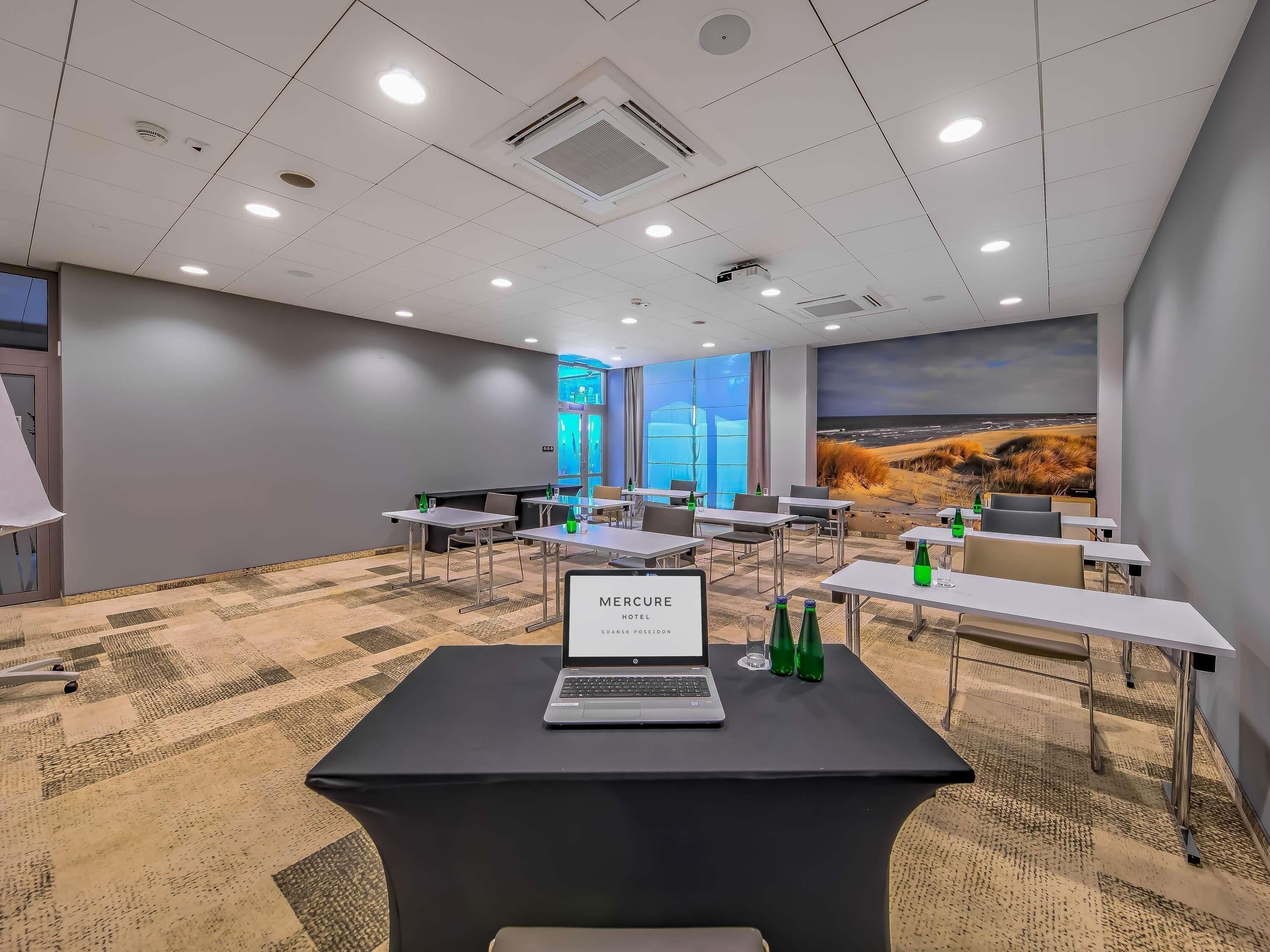 A conference room with tables, chairs, a laptop, and a view of the beach through large windows.