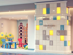 Um hall de hotel com área de recreação colorida, um pilar grande com a marca do hotel e uma parede revestida com ícones do edifício.
