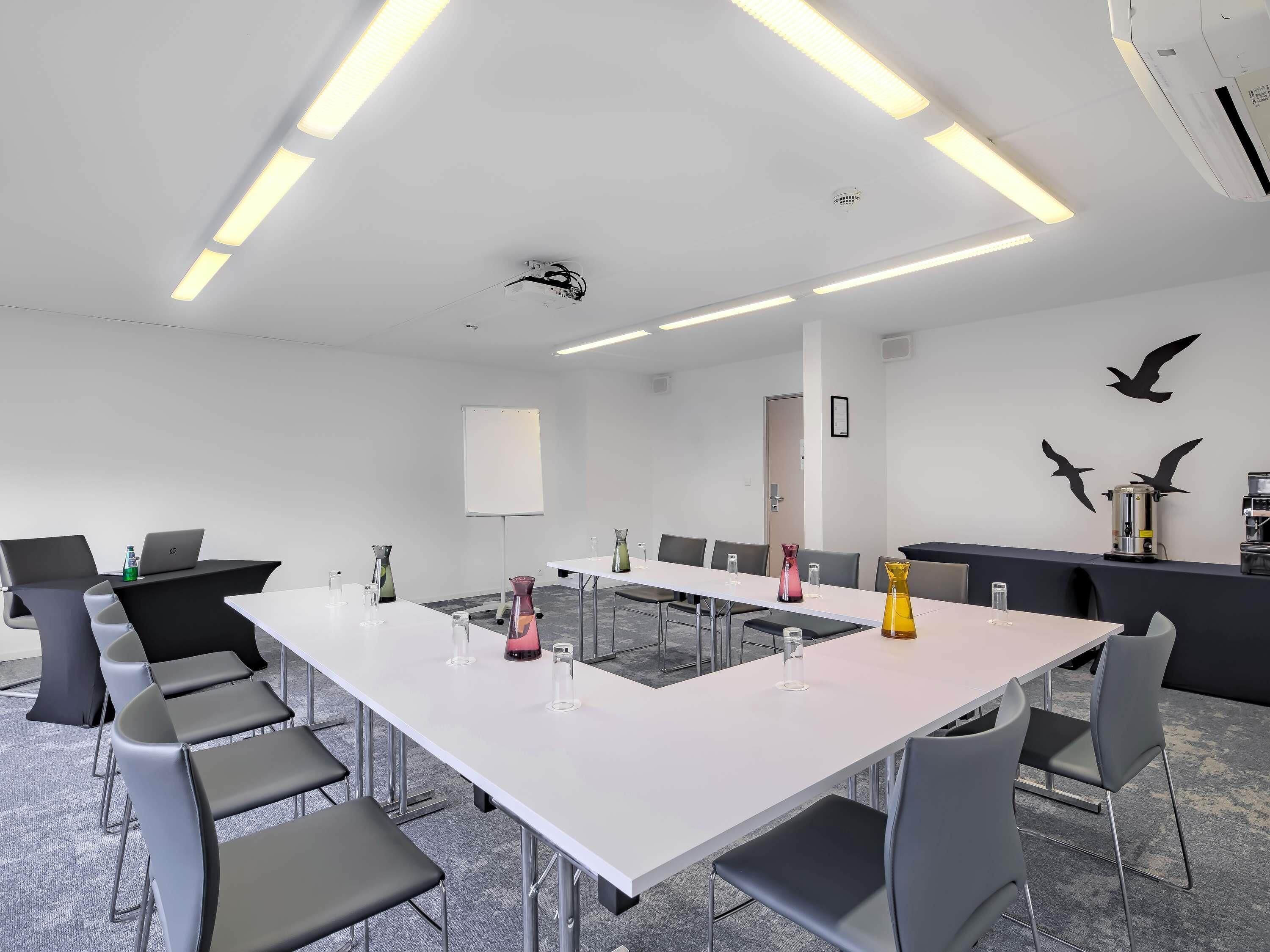 A conference room with a long table, chairs, a projector screen, and a coffee machine.