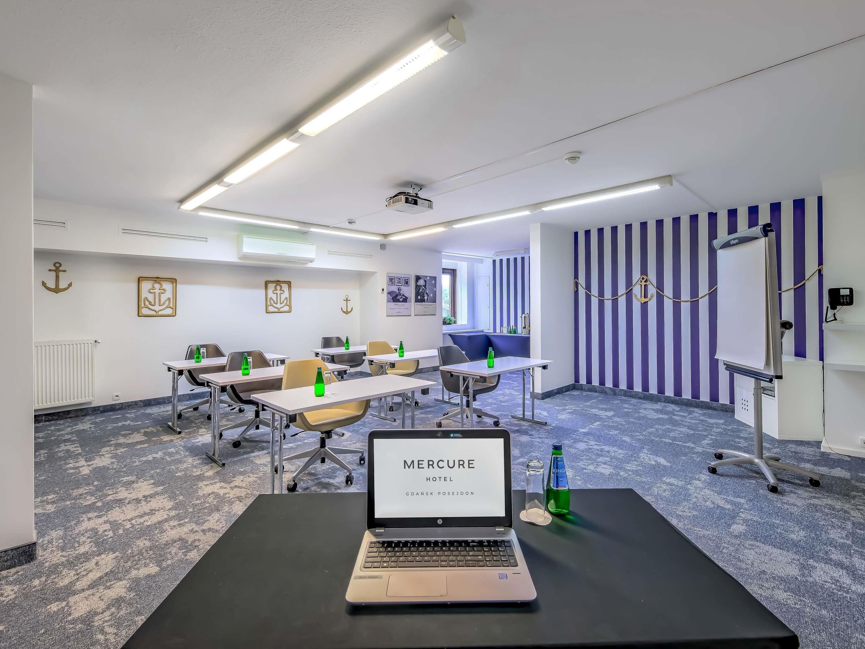 A conference room with tables, chairs, a laptop, and a projector.