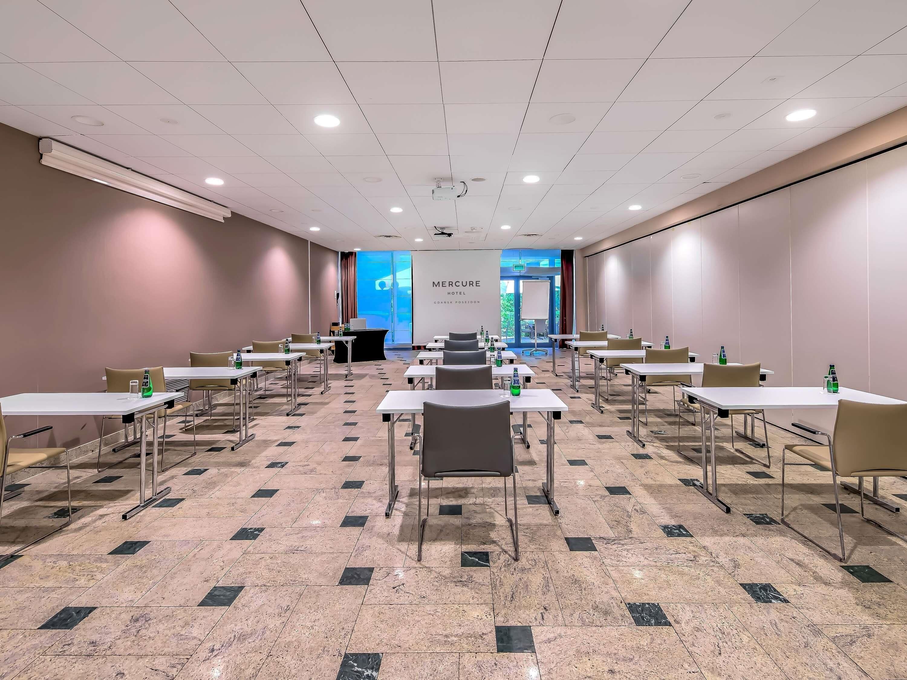 Una sala de conferències amb taules i cadires, un atril i una pantalla gran.