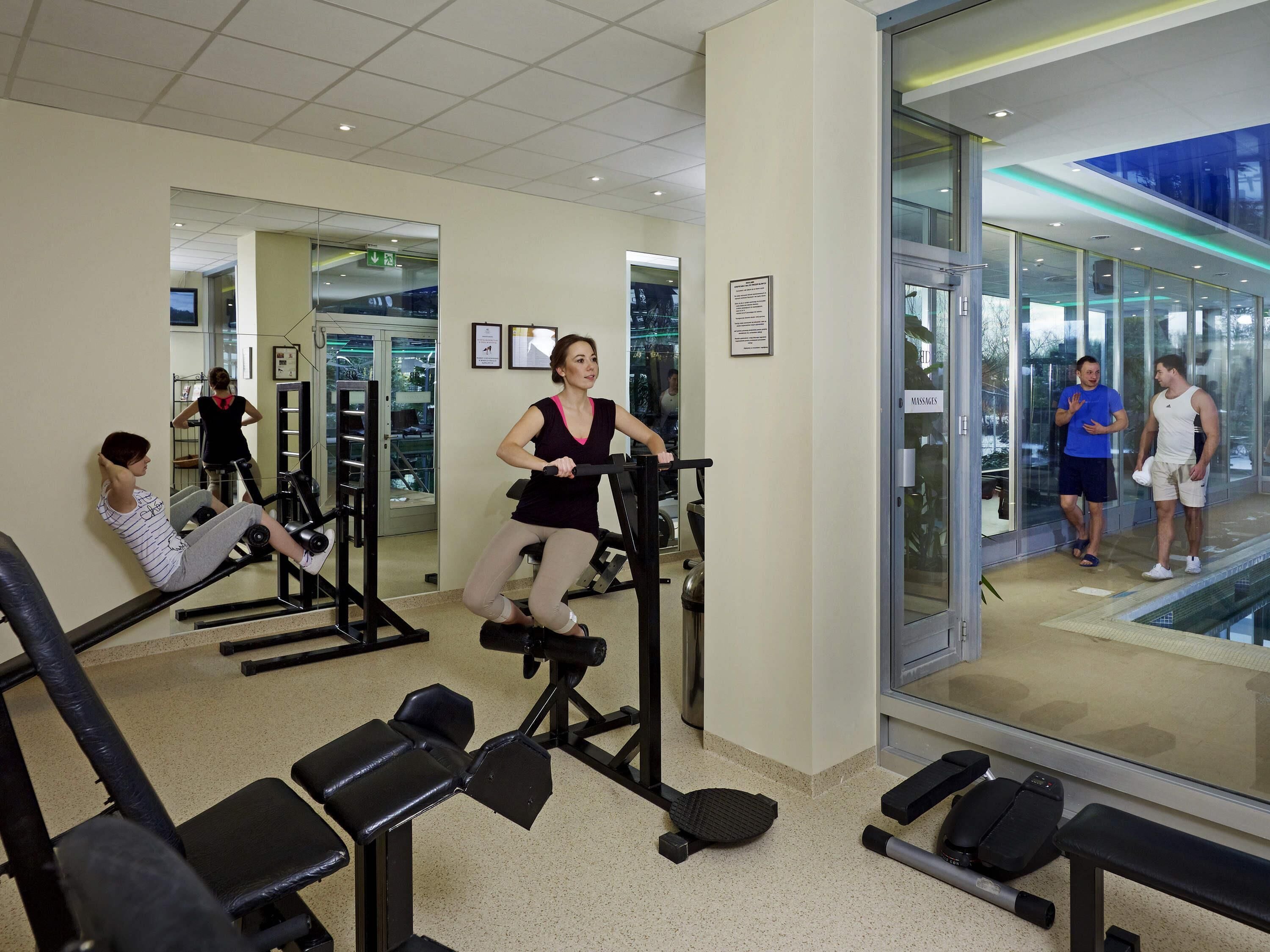 A gym with exercise equipment, mirrors, and a glass wall.