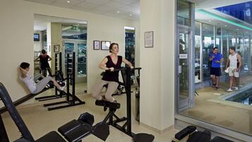 Un gimnasio con equipo de ejercicio, espejos y un muro de cristal.