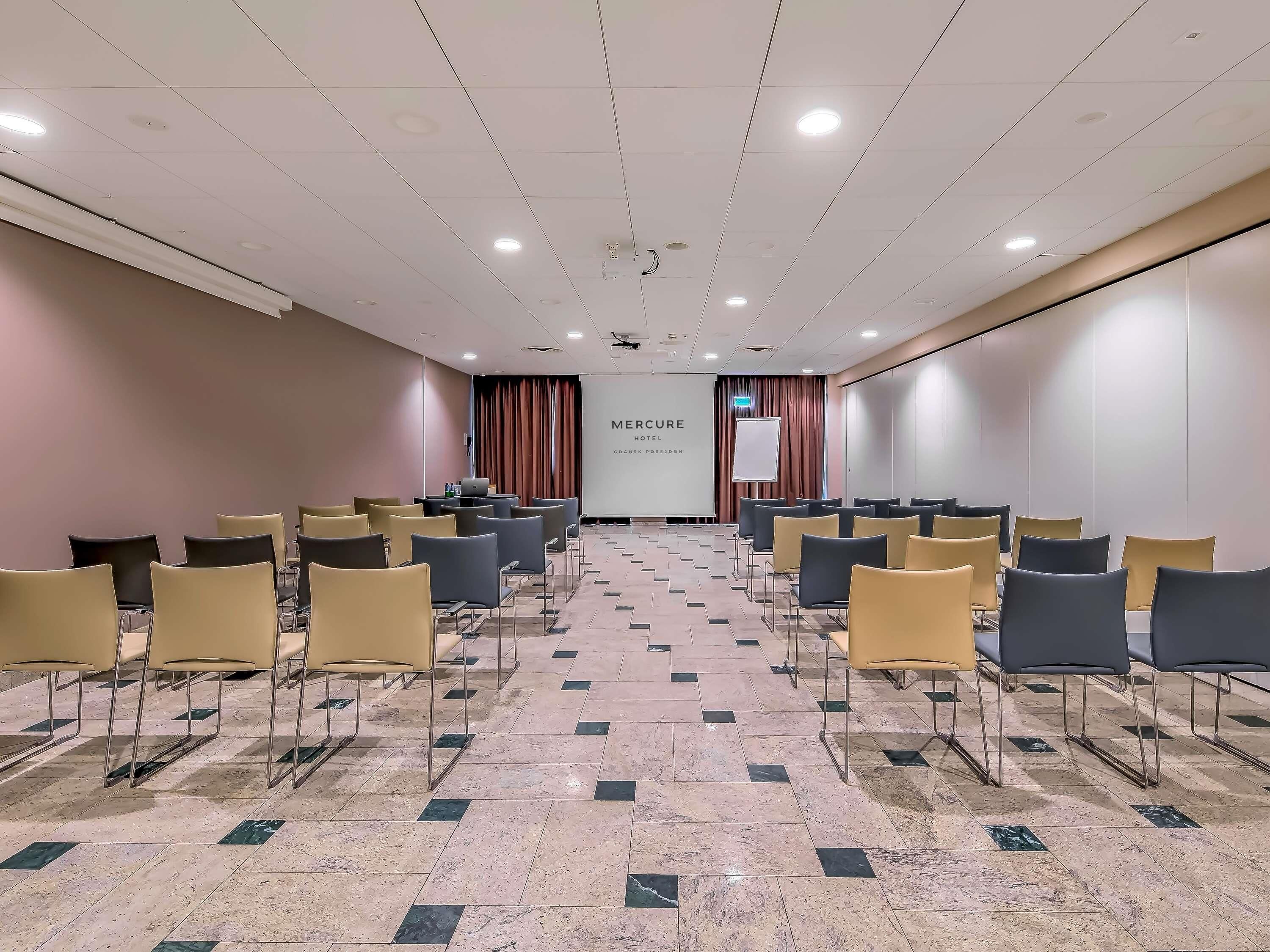 A conference room with rows of chairs, a projector screen, and a presentation screen.