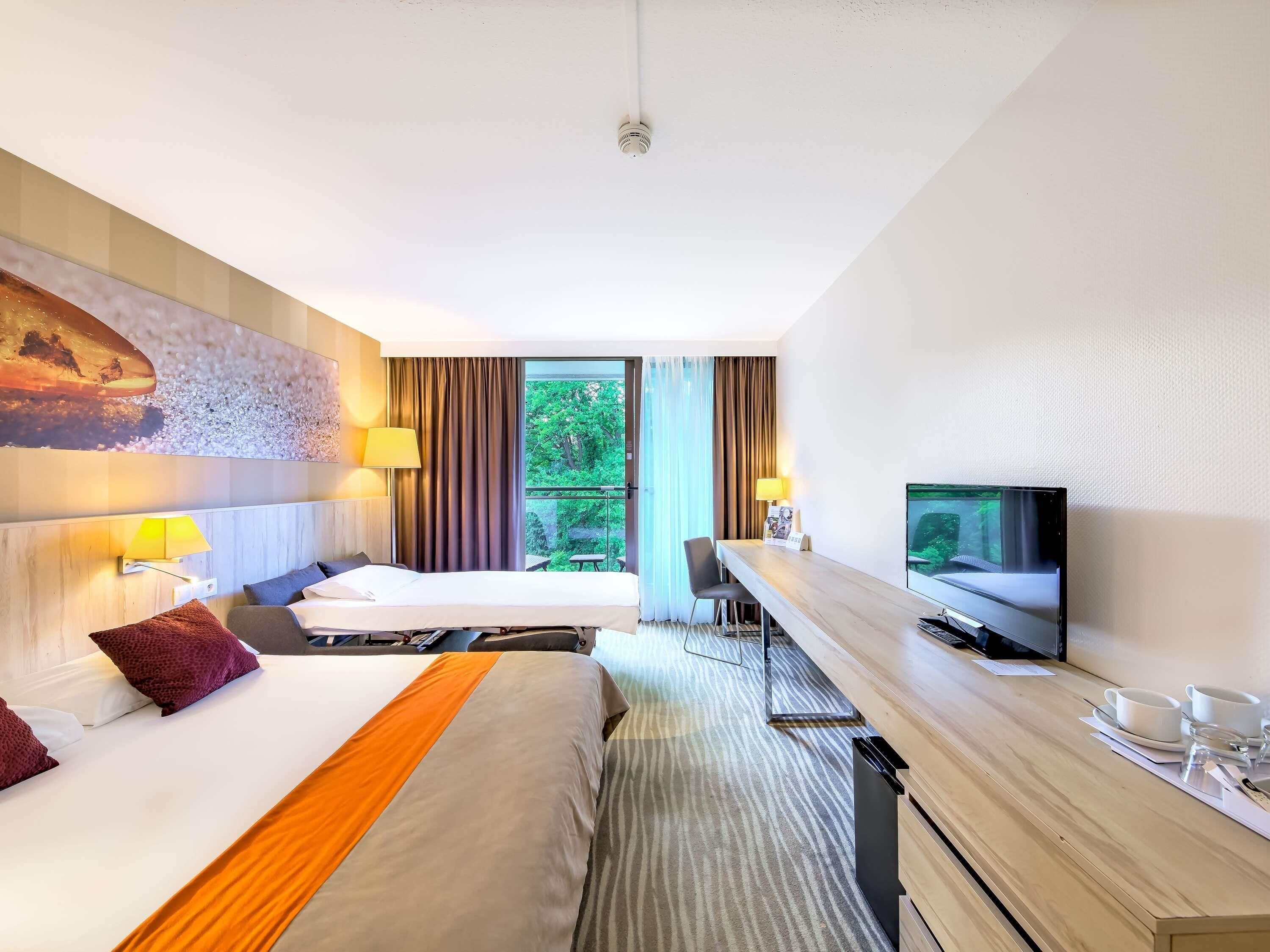 A hotel room with a bed, a desk, a television, and a window with curtains.