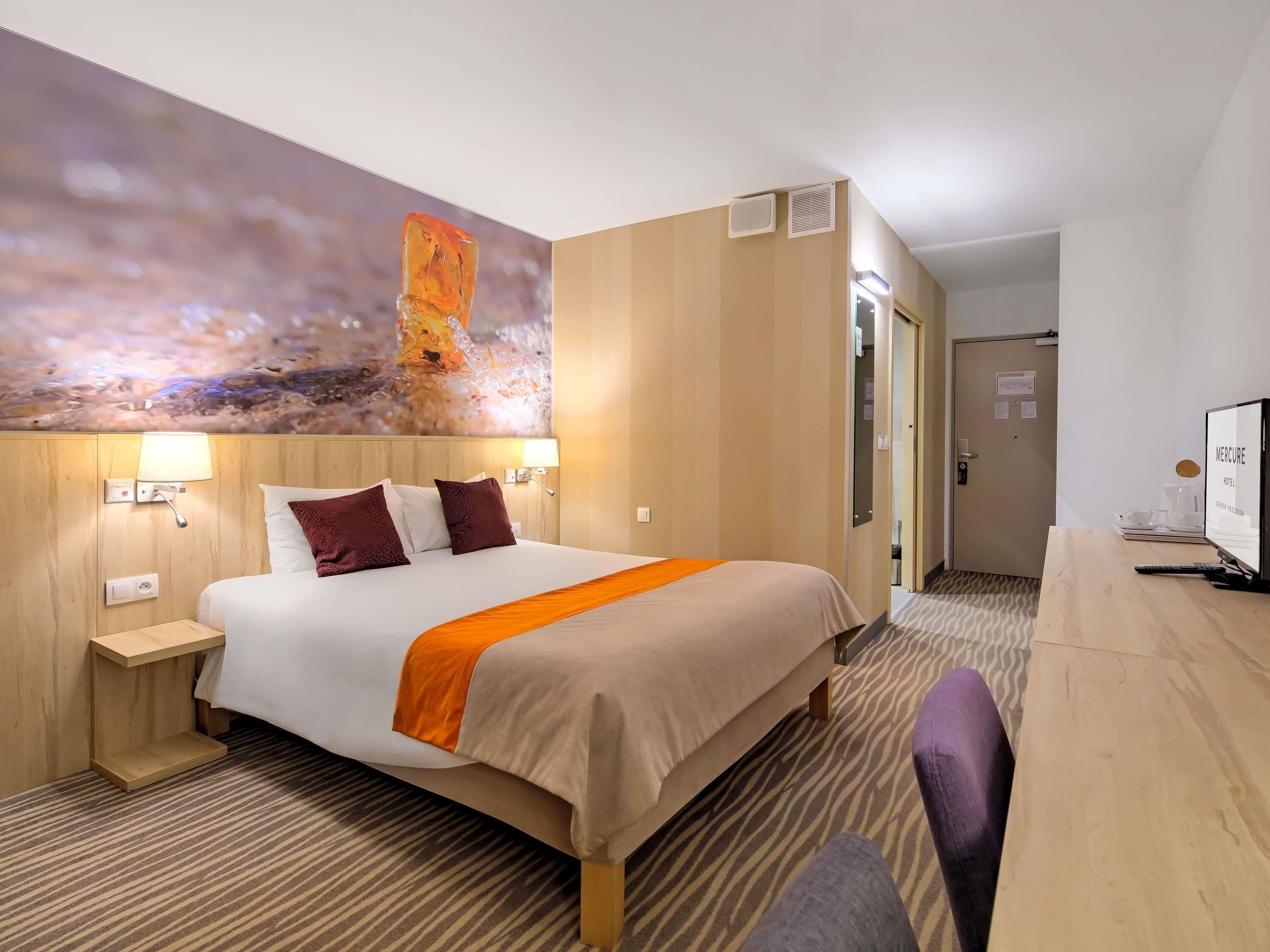 Ein Hotelzimmer mit Bett, Schreibtisch, Fernseher und einem Gemälde an der Wand.