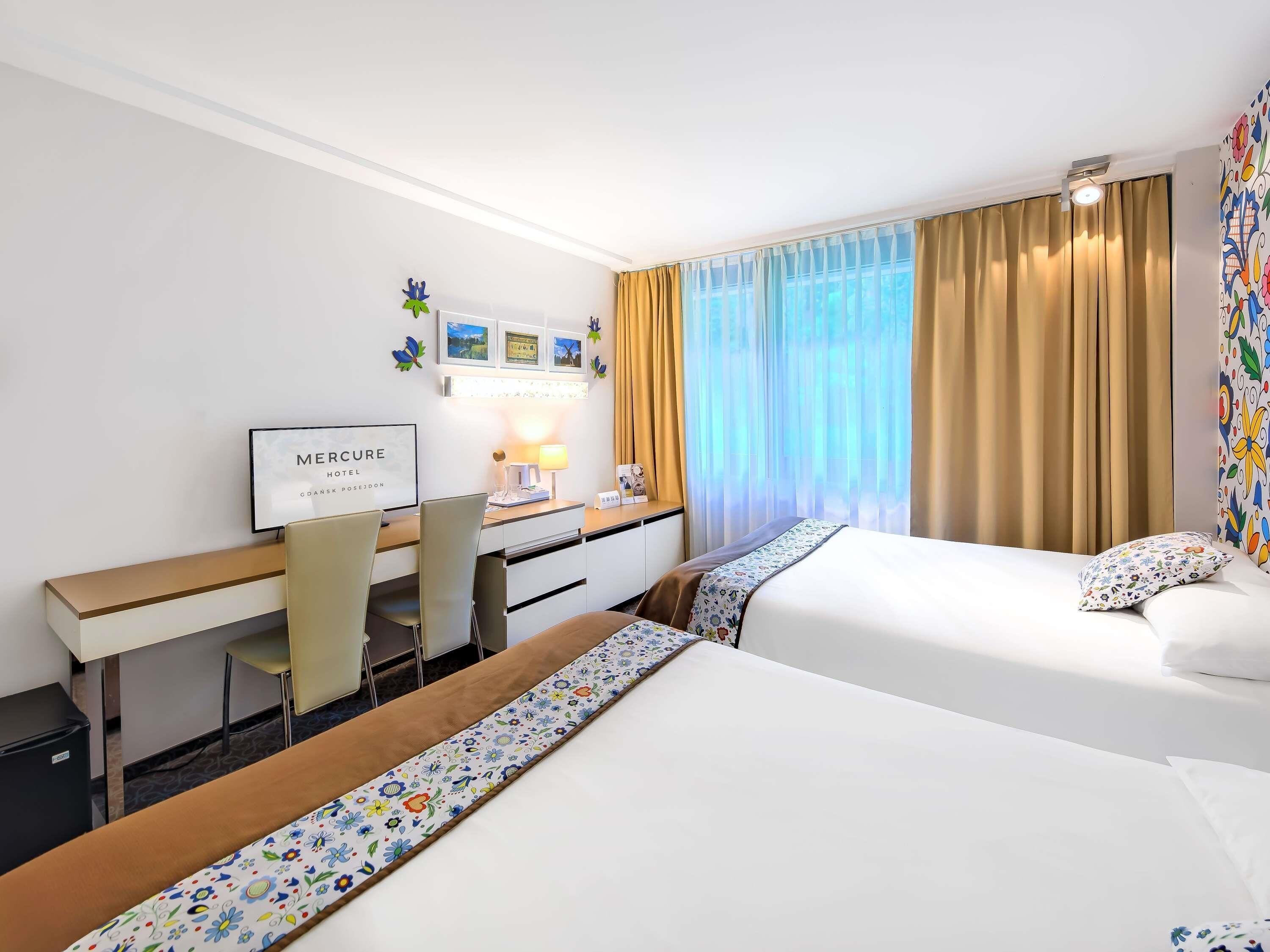 Una habitación de hotel con dos camas, un escritorio, una silla, un televisor y una ventana con cortinas.