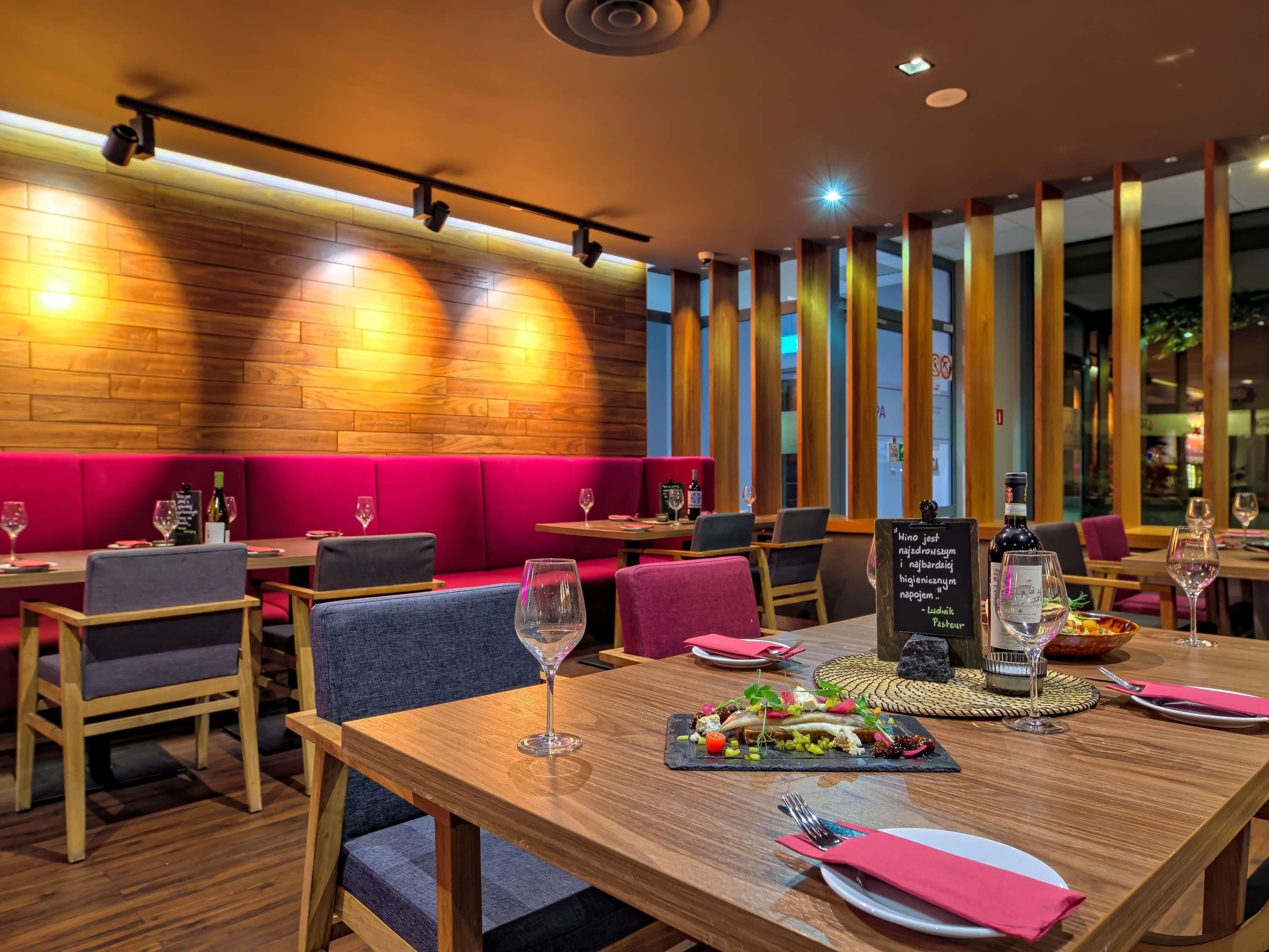 Ein Restaurantinnenraum mit Holzböden, roten Sitzkissen und verschiedenen Tischgestaltungen, darunter Weingläser und Teller.
