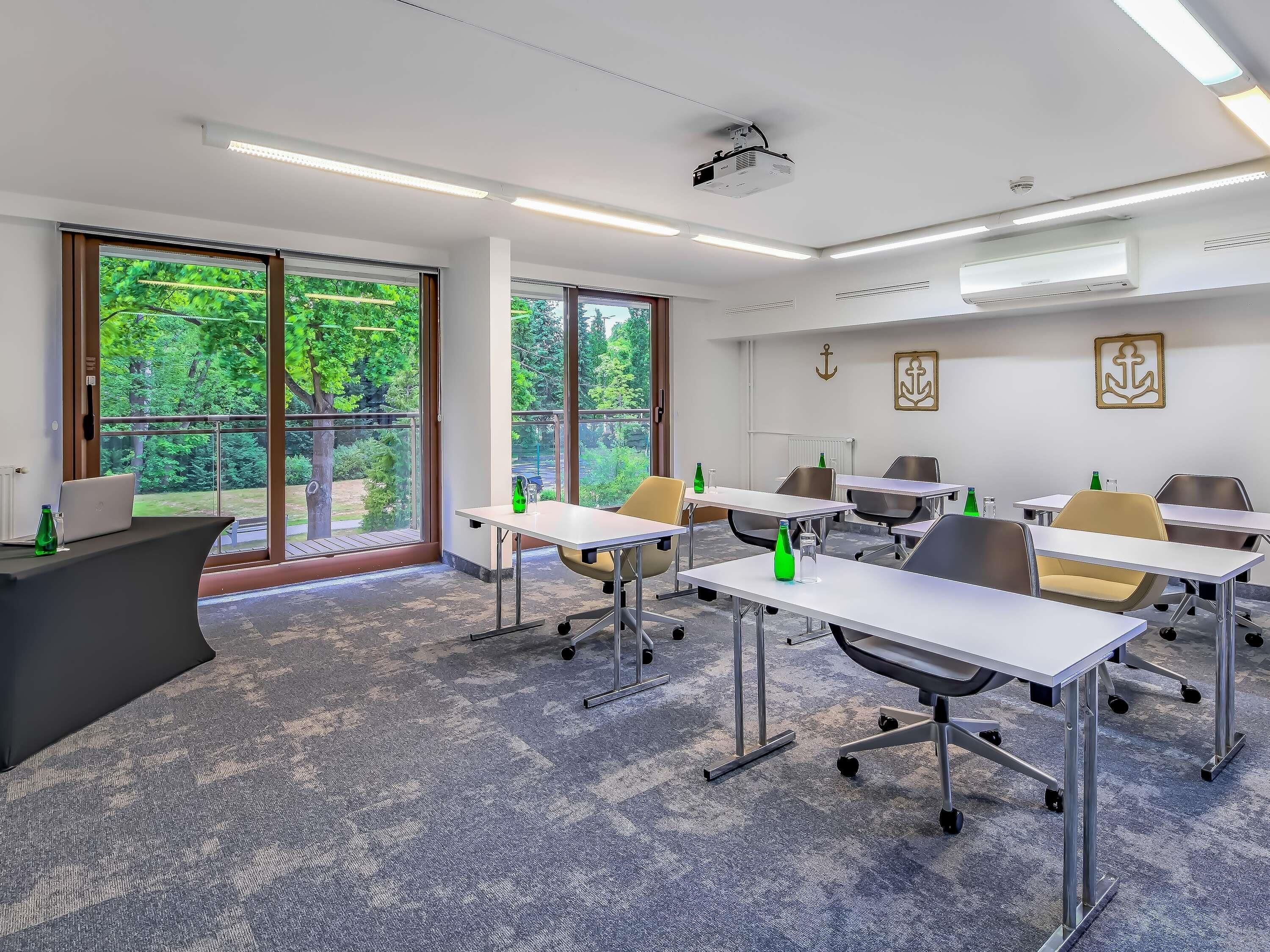 Una sala conferenze moderna con ampie finestre, tavoli bianchi e sedie.