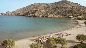 Una playa con agua cristalina, una montaña rocosa al fondo y una fila de tumbonas con sombrillas.