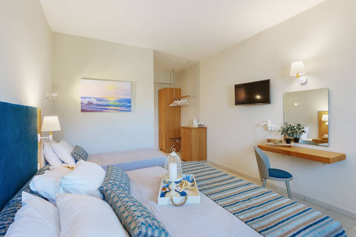 A hotel room with two beds, a desk, a chair, a TV, and a painting of a sunset.