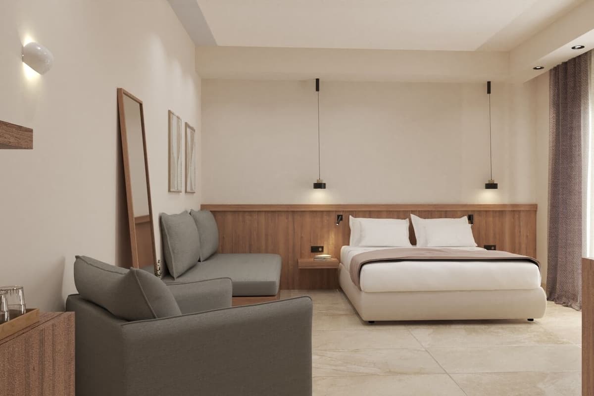 A modern hotel room with a bed, a sofa, a nightstand, and a wall-mounted light fixture.