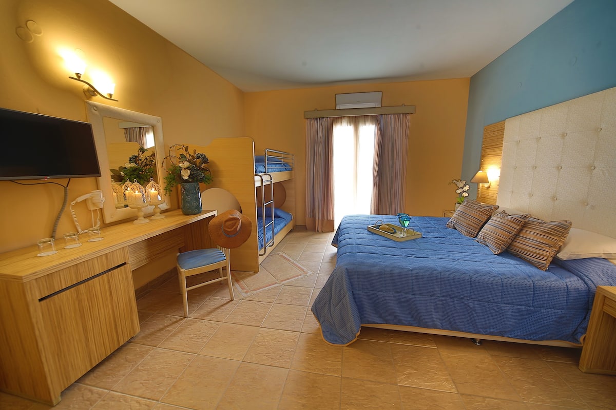 A bedroom with a bed, a desk, a chair, a TV, and a window with curtains.