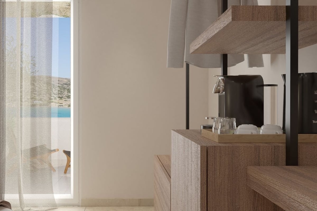 A modern bathroom with a wooden vanity, a coffee machine, and a view of a beach through a large window.