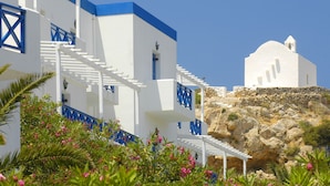 Un edificio blanco con detalles azules y una pared de piedra, que cuenta con una escalera y una pequeña torre de campanas.