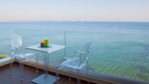 Un balcón con vistas despejadas al mar, con una mesa con velas y dos sillas traslúcidas.