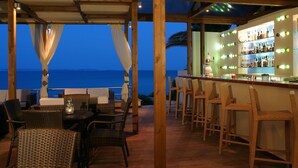 Un área de bar al aire libre con mobiliario de mimbre y vistas al océano.