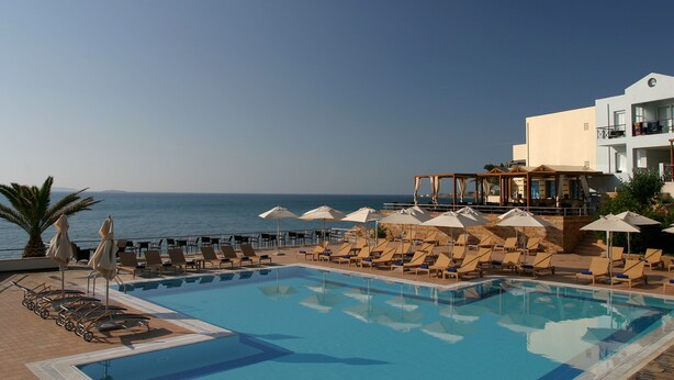 Zona de piscina con sillones de playa y sombrillas, con vista al mar.