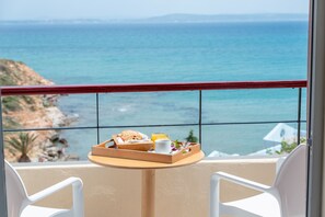 Enjoy a refreshing meal on the balcony with ocean views, featuring a tray with a sandwich, cup, and glass of juice, and two comfortable chairs.