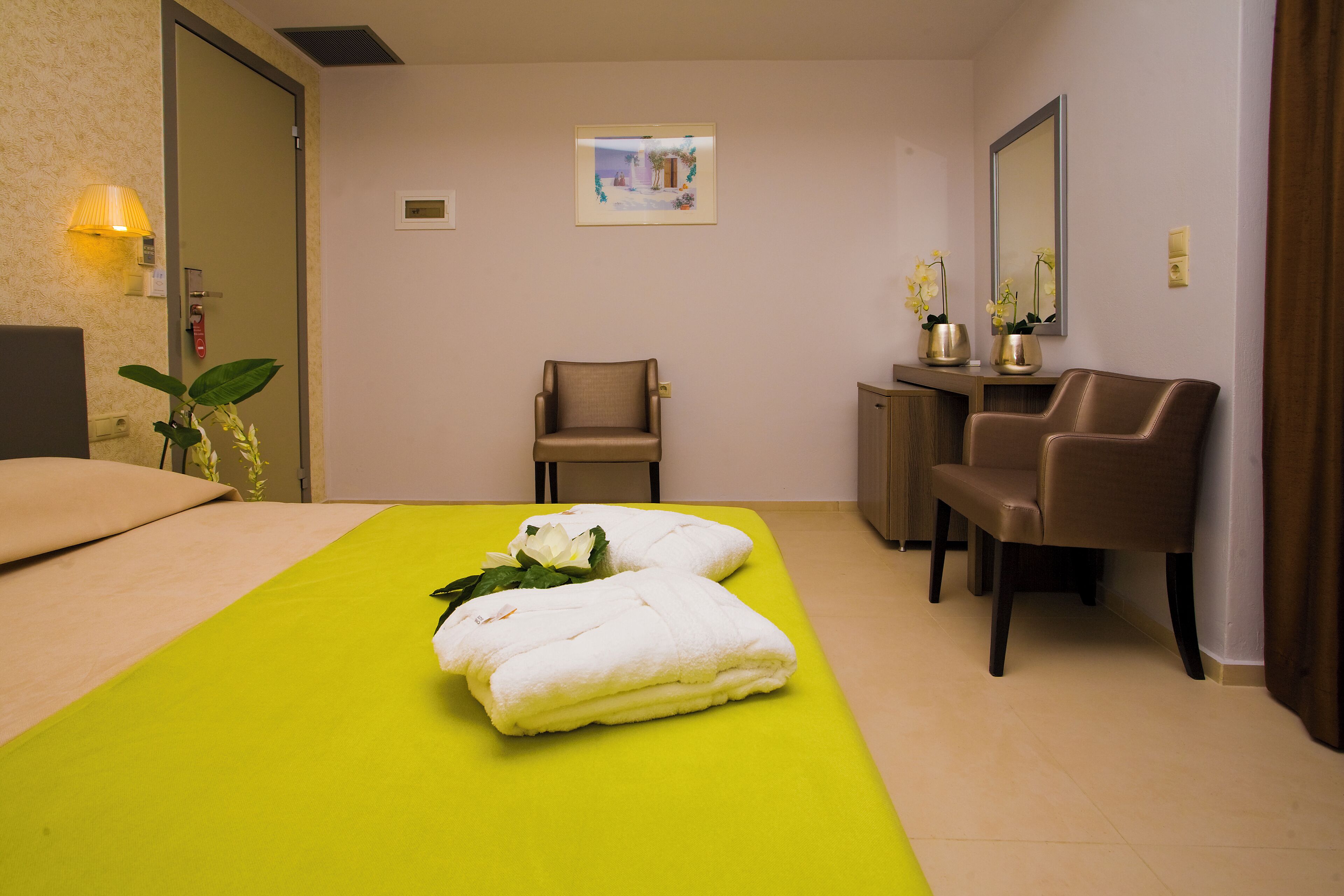 A hotel room with a bed, two chairs, a desk, and a mirror.