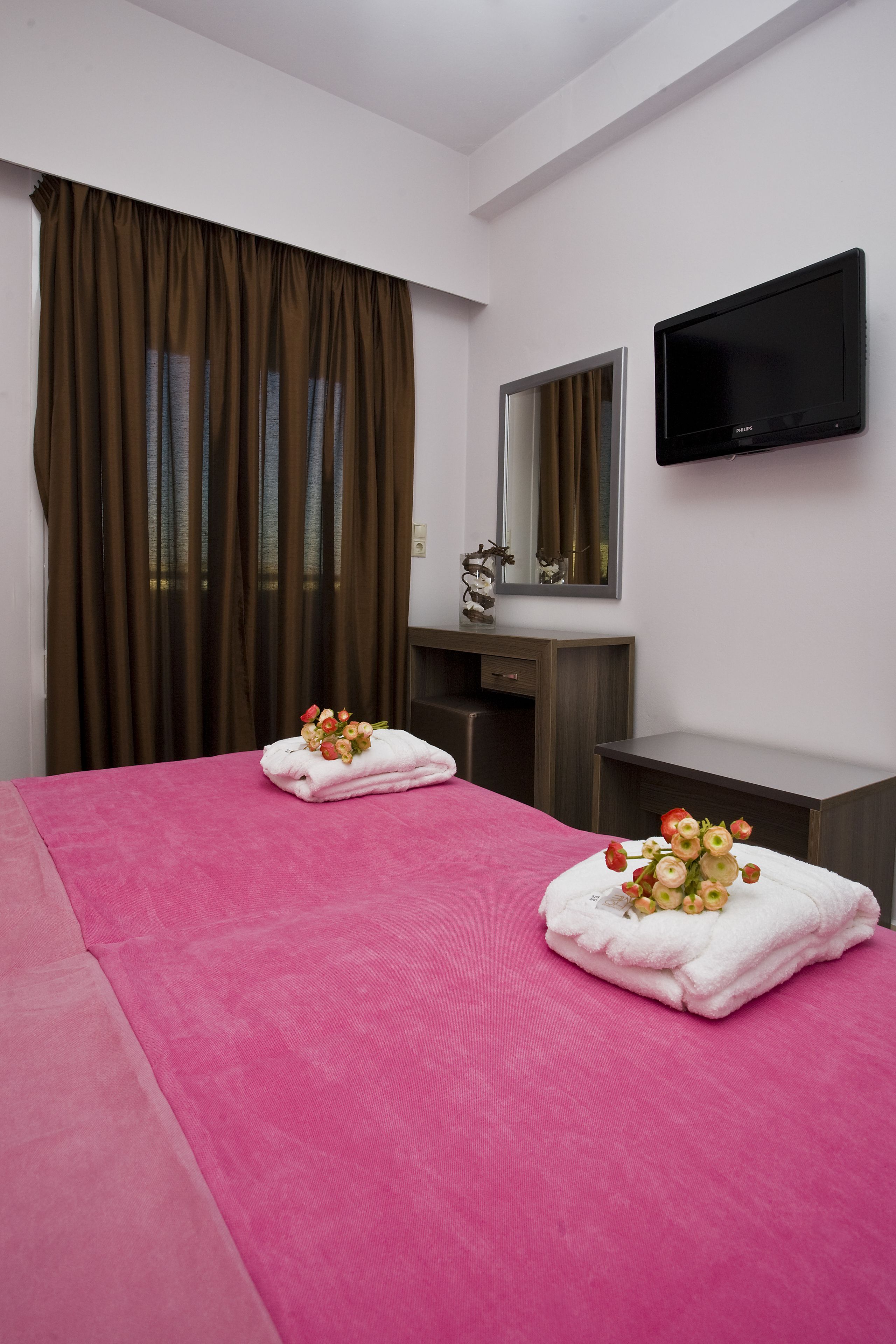 Una habitación de hotel con una cama grande, televisión de pantalla plana, espejo y ventana con cortinas.