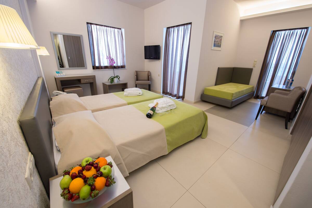 A hotel room with two beds, a desk, a chair, a TV, and a fruit bowl.