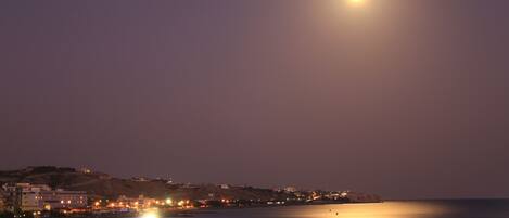A coastal cityscape at night with a visible moon.