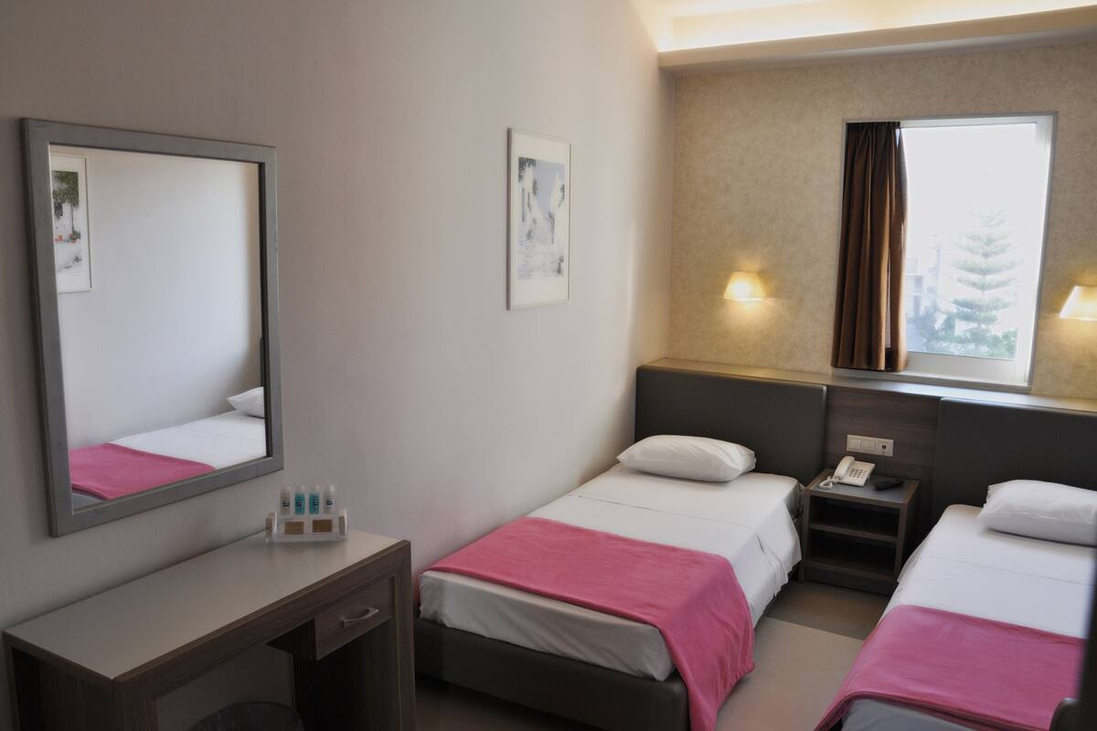 A hotel room with two beds, a desk, a mirror, and a window with curtains.
