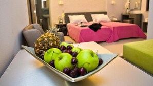 A hotel room with a bed, a bedside table, and a bowl of fruit on a table. - Astron Hotel (Ierapetra)