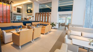 A modern hotel lobby with a seating area, a reception desk, and a large window providing a view of the outdoors. - Astron Hotel (Ierapetra)